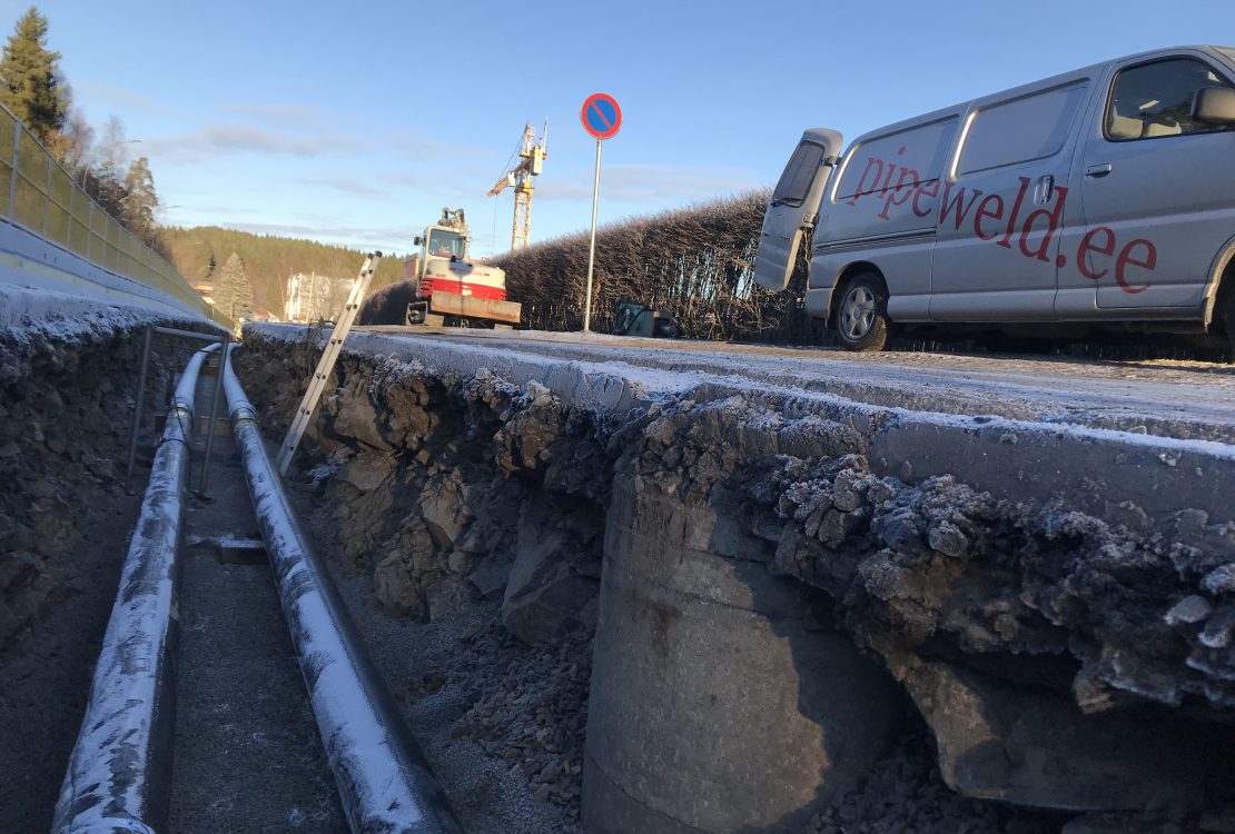 Fjernvarmerør sveiset med gassveising i grøft i Oslo, med firmakjøretøy og logo synlig over grøften.
