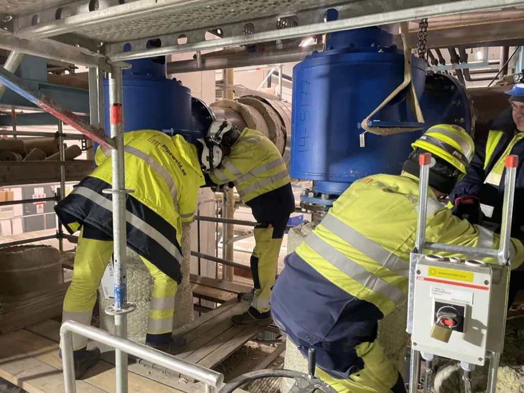 Fyra industriarbetare spänner två stora flänsar på ett industrirör efter packningsbyte.