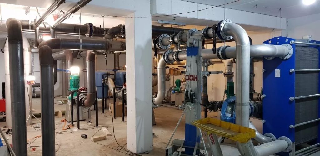 Färdigställt tekniskt rum inom rörmontage med installerade pumpar och kompressor – byggnadens klimatkontrollsystem.