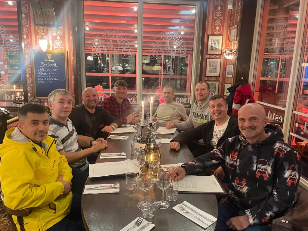 En grupp svetsare inom industrirör firar jul på en restaurang och sitter vid ett dukat bord.