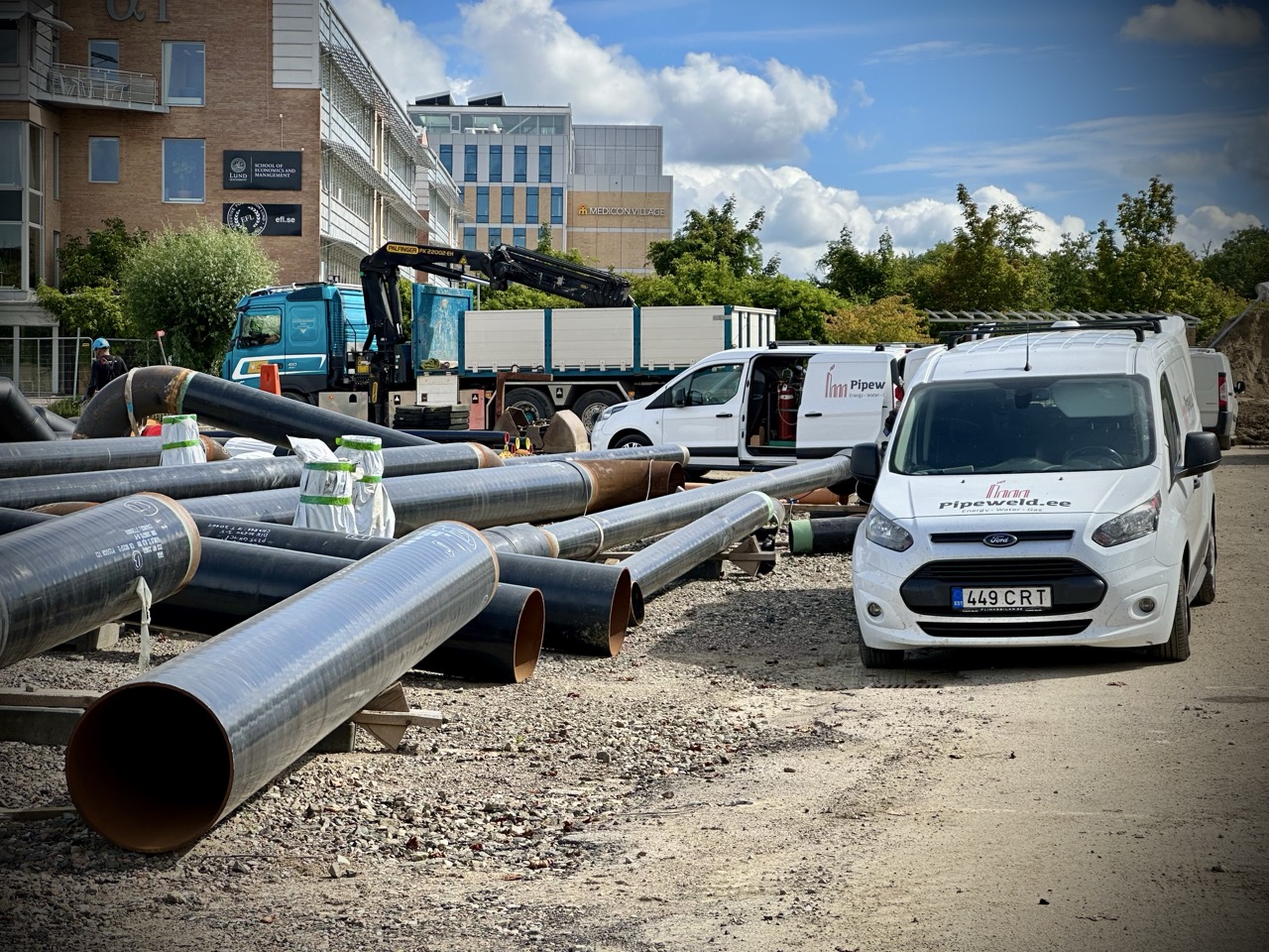 Pipes laid out outdoors, surrounded by vehicles with tools, as preparations for on-site pipe fabrication and prefabrication begin.