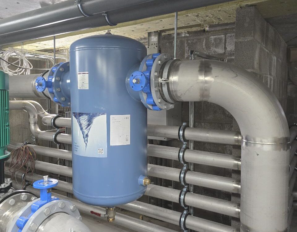 Mechanical contractor installing blue vortex water filtration tank with stainless steel piping system in Oslo, Norway